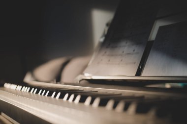 Klavye ve nota kağıdının 88 tuşunun düşük görüntüsü. Yandan gelen ışıkla kapat