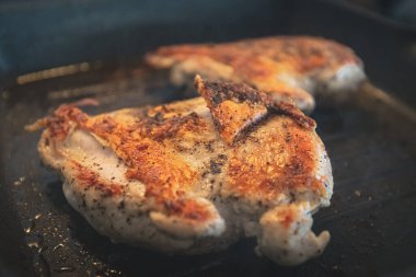 Derisi yüzülmüş çıtır altın tavuk kızgın yağda siyah bir ızgarada kızarıyor.