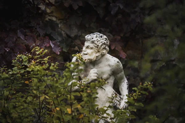 Fehér szobor Pánról, a görög istenről, fuvolával a kezében, lombozat mögé bújva, pimaszul néz ki. Stock Kép