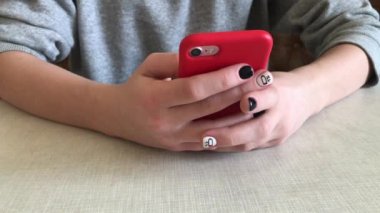 Kız parmak bir cep telefonu ekran dokunur. Bir kız ile bir telefon onun elinde bir masada oturur.