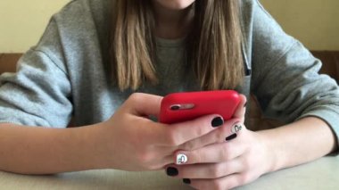 Kız parmak bir cep telefonu ekran dokunur. Bir kız ile bir telefon onun elinde bir masada oturur.