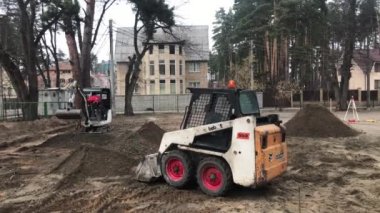 Operasyonda iki Traktörler. Tarak yere kazıyor. İşçi ağır makine üzerinde çalışıyorum. İnşaatçılar kaldırım döşeme döşenmesi için toprak seviye.