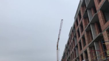 Çok öykülü, tuğla bina inşaatı. Vinç yapı malzemeleri kaldırıyor. Binanın çatı inşaatçılar.