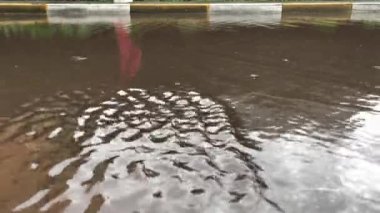 Su birikintisindeki bir adamın yansıması. Yağmurdan sonra su akışı. Sokağın aşağısında yağmur suyu akıyor. Bulutlu hava.