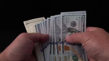 Adam siyah bir arka plan üzerinde dolar sayar. Bir adamın elinde bir demet Amerikan parası. Sahte bir banknot için 100 dolarlık banknotları kontrol ediyorum. Kavram: zenginlik, zenginleştirme, sahte para doğrulama.