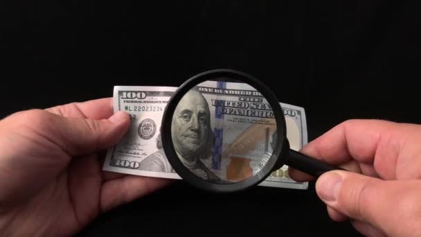男は虫眼鏡を通してドルをチェックします 男の手には虫眼鏡と100米ドルです 額面100ドルの紙幣を偽物でチェックする — ストック動画