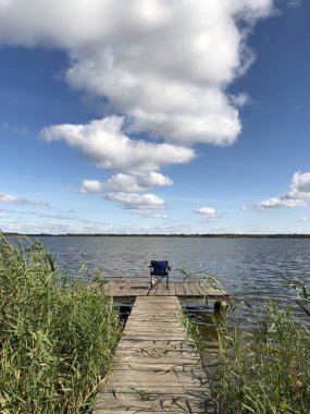 Göldeki balıkçı iskelesi. Gölette balık tutmak için köprü. Nehir kıyısındaki balıkçılar için ahşap bir platform. Bulutlar ile mavi gökyüzüne karşı gölün güzel görünümü