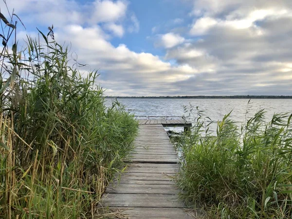 Muelle de pesca en el lago. Puente para pescar en el estanque. Plataforma de madera para pescadores junto al río. Hermosa vista del lago contra el cielo azul con nubes —  Fotos de Stock