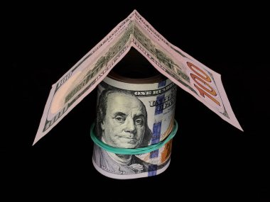 100 Amerikan dolarının banknotları bir ev şeklinde katlanır. Amerikan parası siyah bir arka planda elastik bir bantla sarmalanmış. Konsept: Gayrimenkul yatırımı