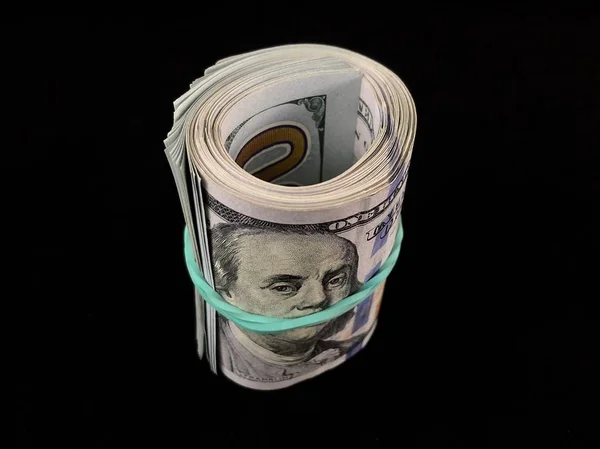 Banknoten zu 100 US-Dollar auf schwarzem Hintergrund. Hundert-Dollar-Scheine werden mit einem Gummiband verdreht. Amerikanisches Geld auf dem Tisch. — Stockfoto