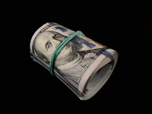 Banknoten zu 100 US-Dollar auf schwarzem Hintergrund. Hundert-Dollar-Scheine werden mit einem Gummiband verdreht. Amerikanisches Geld auf dem Tisch. — Stockfoto