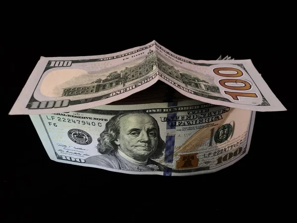 Banknoten im Wert von 100 US-Dollar werden in der Form eines Hauses gefaltet. amerikanisches Geld auf schwarzem Hintergrund. Bild von Präsident Franklin auf Dollars. — Stockfoto