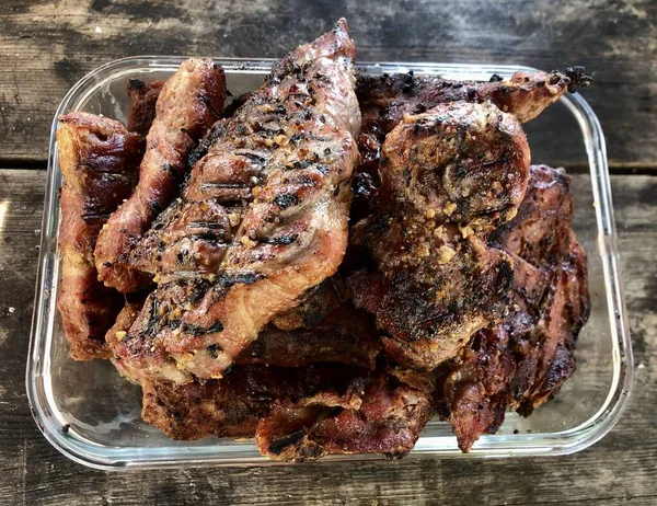 Biefstuk in een glazen kom op een donkere tafel. Geroosterd vlees ligt op een bord, op een houten tafel. Smakelijke steaks gekookt in de natuur. — Stockfoto