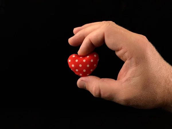 Roodhartje in de hand van een man. Een man houdt een teder hart vast met zijn vingers. Liefde in mannelijke handen, op een zwarte achtergrond. Concept: liefde en passie — Stockfoto