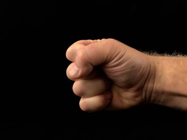 Yumruk savaşa hazır, siyah arka planda. Parmaklar sıkıca kenetlendi. Güçlü adam yumruğunu kaldırdı. Kavram: saldırganlık, güç, protesto