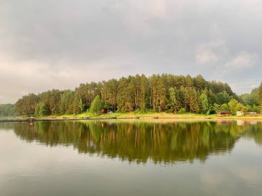 Ağaçlar gölün suyuna yansıyor. Akşam manzarası, ormanda küçük bir gölet. Mavi gökyüzünün yansıması ve bir park rezervuarındaki ağaçlar. Doğanın ortasında bir gölette gün batımı.