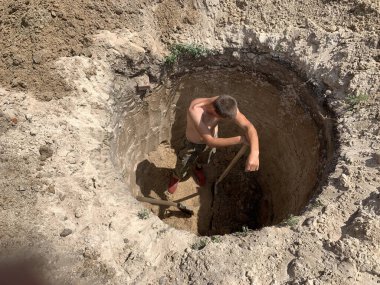 Derin bir deliğe kürek sokan bir adam. Bir işçi yerde bir çukur kazar. Adam kuma bir çukur kazdı..