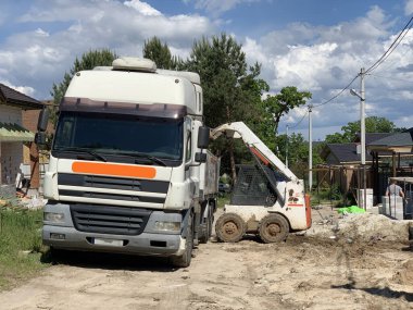 İnşaat alanında ağır makineler. Yükleme sırasında yükleyici ve kamyon. İnşaat malzemelerini kazıcıyla boşaltıyorum. Irpin, Kiev bölgesi, bir ev inşaatı, 15 Ağustos 2020
