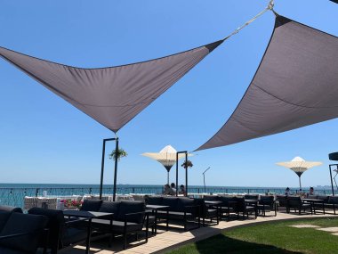 Deniz kenarındaki bir kafede güneş koruması. Okyanusa bakan rıhtım restoranı. Kumaş kaplı deniz kenarındaki masalar. Odessa, 10 Temmuz 2020 'de baraj kenarında bir büfe.