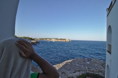 Etrafında havlu olan kimliği belirsiz bir çocuk okyanusa bakıyor.