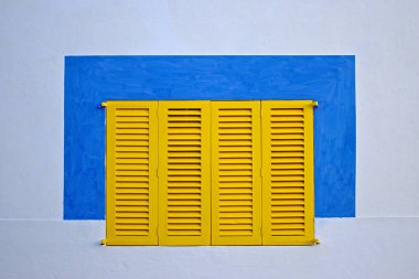 Sarı pencereli beyaz bir duvar ve etrafında mavi bir kare var.