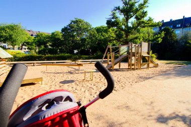 Güneşli bir günde, kum havuzu ve küçük ahşap evleri olan bir oyun parkının yanında gezinen.