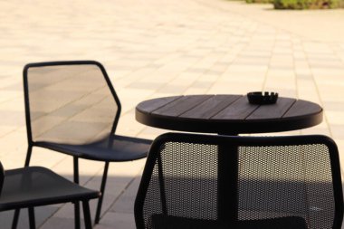 Sandalyeler, gölgede kül tablası ve güneşli bir arka plan.