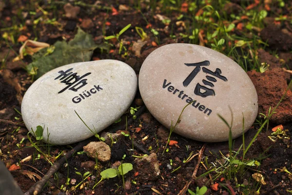 Two stones on the ground with asian ideographs and german words saying trust and luck