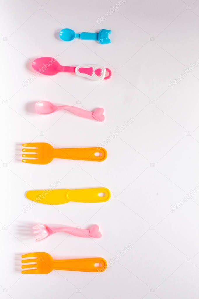 Children plastic dishes on a white background, forks, spoons, plate with space for text. Flat lay, top view minimal concept.