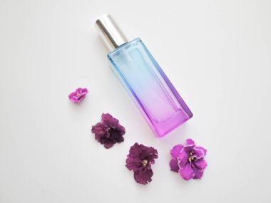  Etrafında çiçekler olan mor parfüm şişesi. Lavanta ve bahar çiçeği aroması, aromaterapi, spa konsepti, cilt bakımı.