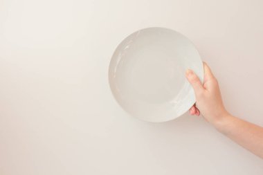  Kadın el, beyaz arka planda beyaz yuvarlak bir plaka tutar. Kopya alanı olan bir model gibi. Seramik düz daire