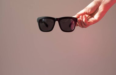  Siyah stil klasik güneş gözlüğü. Güneşin altında gri bir arka planda bir el. Metin için kopyalama alanı olan kart.