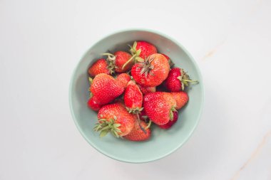 Beyaz mermer bir masada yeşil seramik tabakta çilekler. Metin için kopyalama alanı olan kart. Üst görünüm, düz görünüm.