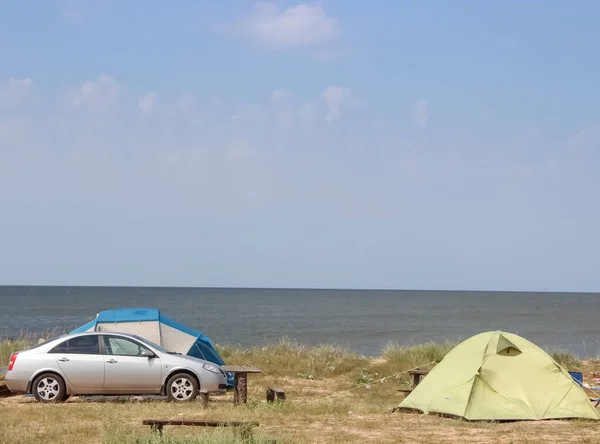 Holidays at sea with a tent, a family camp on the shore of the Sea with a car, a wooden table and a bench.