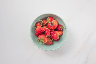 Beyaz mermer bir masada yeşil seramik tabakta çilekler. Metin için kopyalama alanı olan kart. Üst görünüm, düz görünüm.