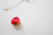 Eine reife rote Erdbeere auf einem Tisch aus weißem Marmor. Stilvolle Fotoarbeiten, Minimal- und Sommerkonzept, Sommerbeeren. 