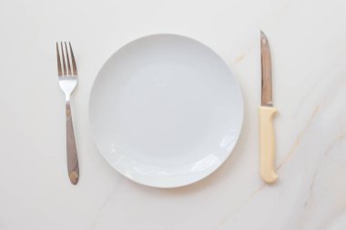  Boş beyaz tabak, mermer bir masa, çay tabağı, çatal ve bıçak. Diyet kavramı, oruç tutmak..