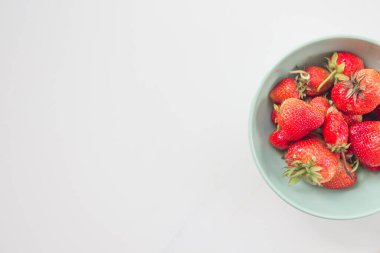  Beyaz bir masada, üzerinde fotokopi alanı olan seramik yeşil bir tabakta sulu, çevre dostu çilekler. Üst Manzara. Düz yatıyordu