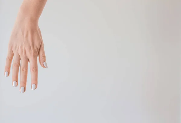 Mano femenina con una hermosa manicura sobre un fondo de una pared blanca. Piel delicada y saludable en las manos, rejuvenecimiento de la piel de las manos, hidratación y cuidado —  Fotos de Stock