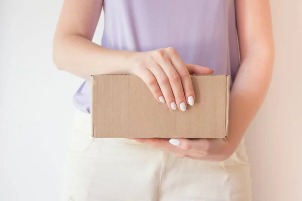 Beautiful girl with a parcel in hands, delivery concept. White manicure, box with order.