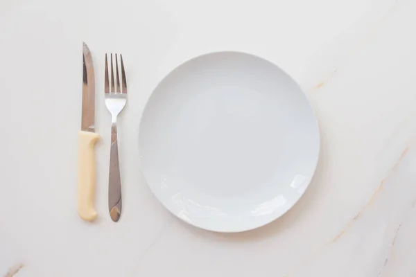 Placa branca vazia com talheres em uma mesa de mármore, pires, garfo e faca. O conceito de dieta, jejum — Fotografia de Stock