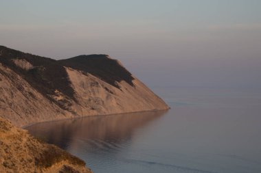  Gün batımında mavi deniz suyuyla kaplı güzel bir uçurumu olan bir körfez. Okyanus kıyısındaki kayalar, kayalık çıkıntı, uçurum.