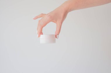 Beyaza izole edilmiş bir kadın elinde plastik krema kavanozu. Cilt gençliğini ve yaşlanma önleyici kremi yenilemek için profesyonel kozmetik ürünler. Deri bakımı konsepti. Kavanoz modeli