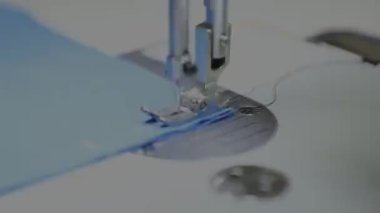 Dikiş makinesinin büyük gümüş iğnesi mavi kumaş üzerinde çalışır.