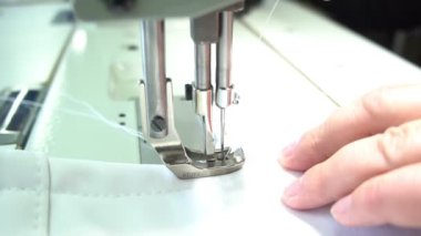 Profesyonel terzi elektrikli makineyle beyaz kumaş dikiyor