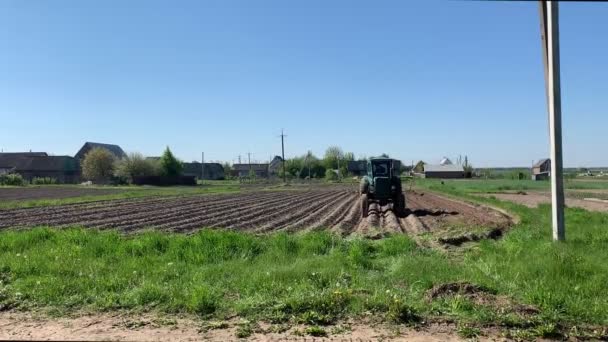 Trattore guida terreno straziante sul campo agricolo contro villaggio — Video Stock