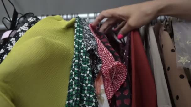 Mujer con manicura rosa ordena la ropa que cuelga en el estante — Vídeos de Stock