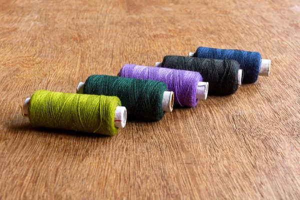 Black, deep green and deep blue colored sewing thread spools on brown wooden background. Close up and side view.