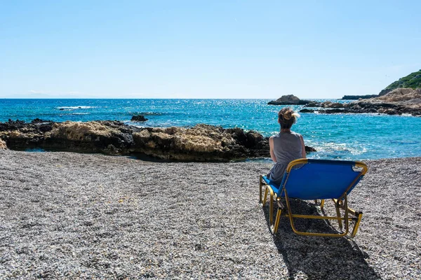 Kobieta w fotelu na kamienistej plaży. — Zdjęcie stockowe