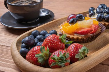 ahşap bir tabak ve masada kahve fincan üzerinde meyve tartlets,
